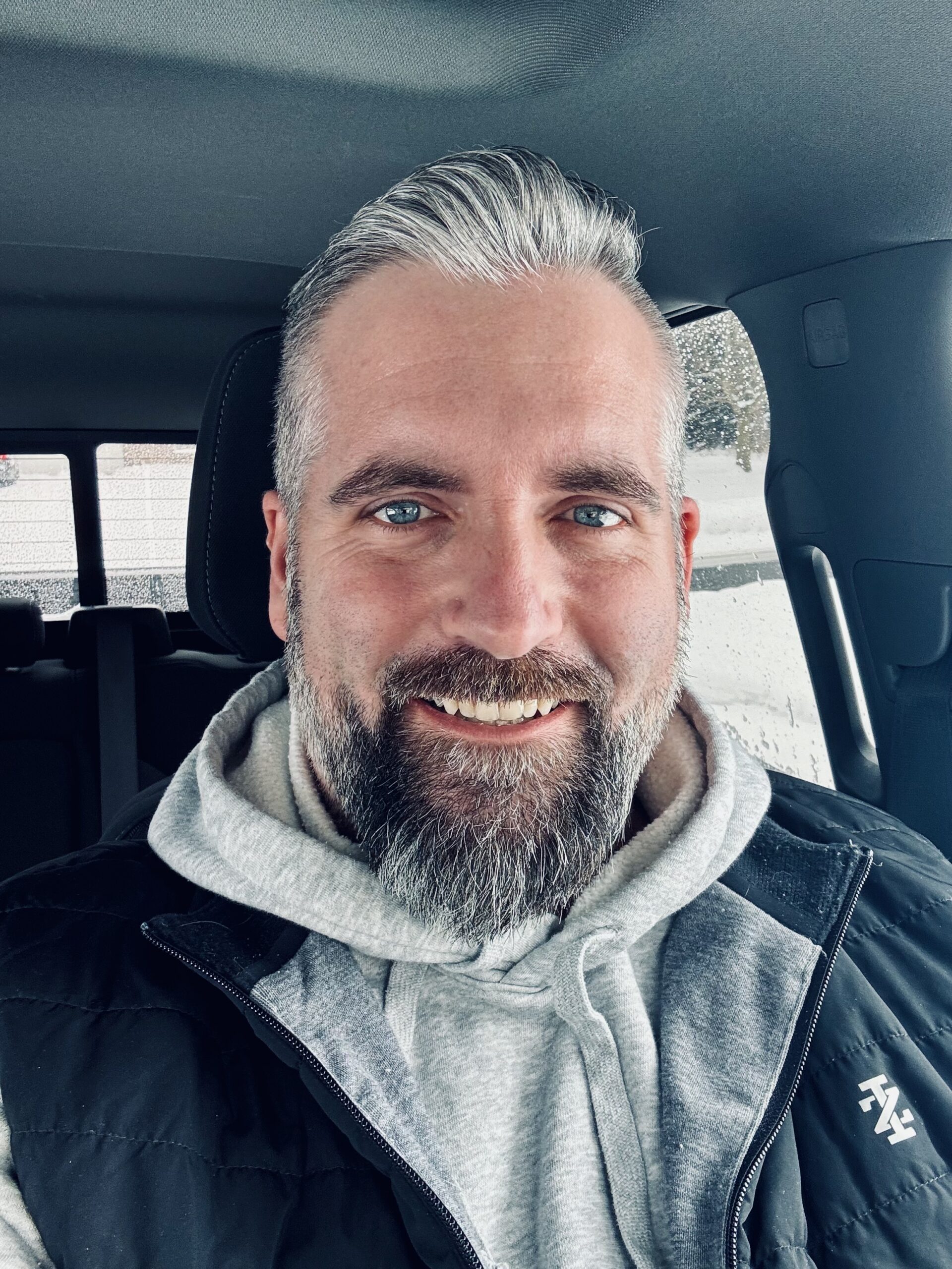 A man with gray hair and beard sitting in the back of a car.