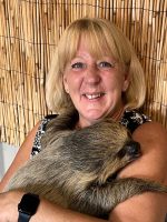 A woman holding a baby raccoon in her arms.